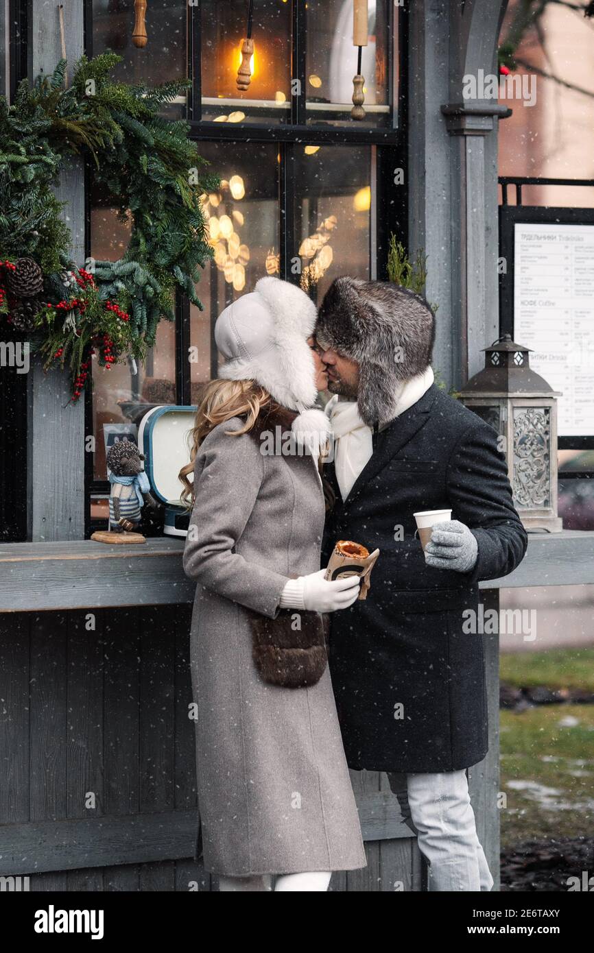 Couple of lovers kissing, stands at street cafe in winter, hugging, drinking hot drinks. Stock Photo