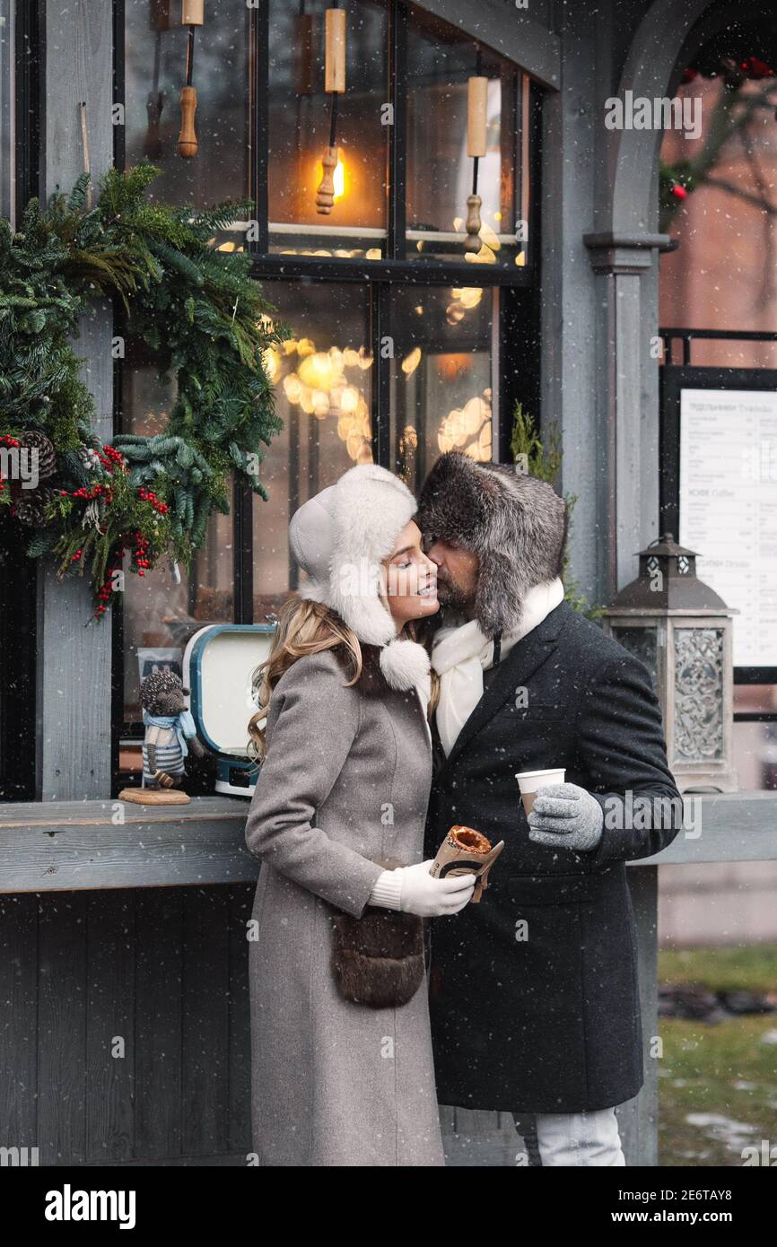 Couple of lovers kissing, stands at street cafe in winter, hugging, drinking hot drinks. Stock Photo