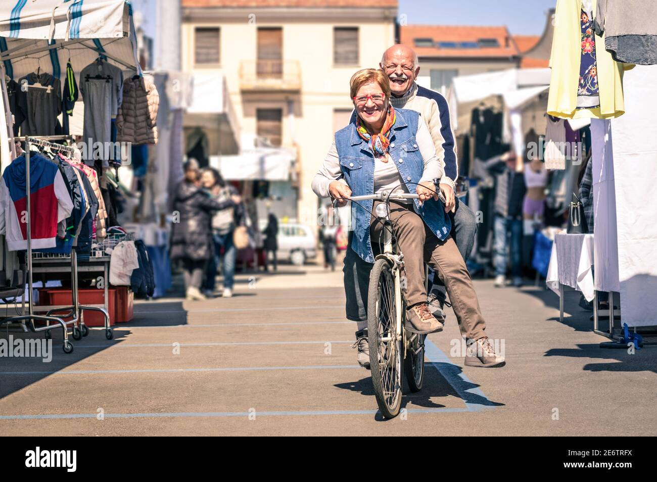 Happy senior couple having fun with bicycle at flea market - Concept of active playful elderly with bike during retirement - Everyday joy lifestyle Stock Photo