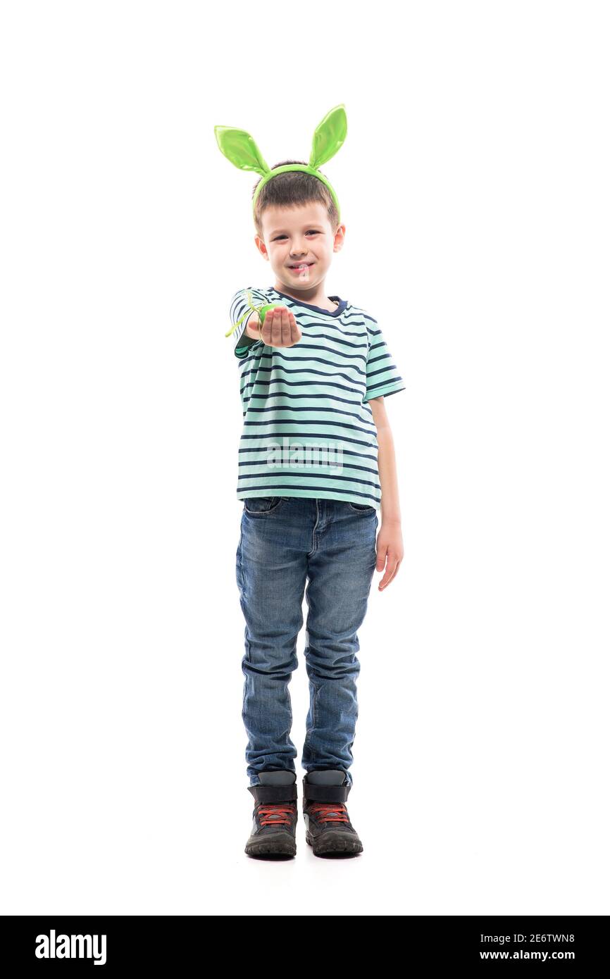 Cute young boy giving Easter egg with forced smile looking at camera. Full length isolated on white background. Stock Photo