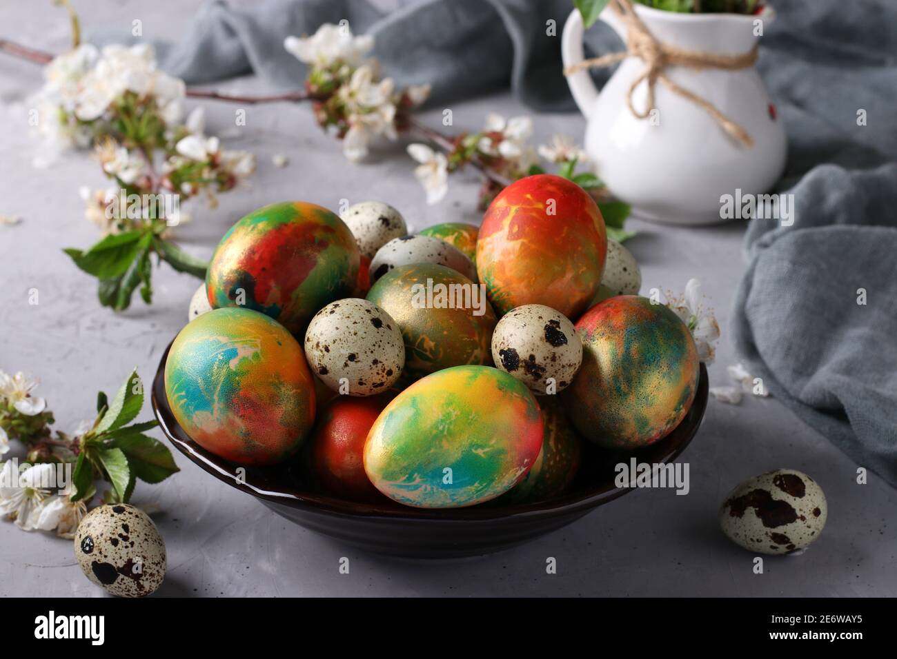 Marble Easter eggs painted with multi-colored food colors and quail eggs in a plate on a gray background. Stock Photo