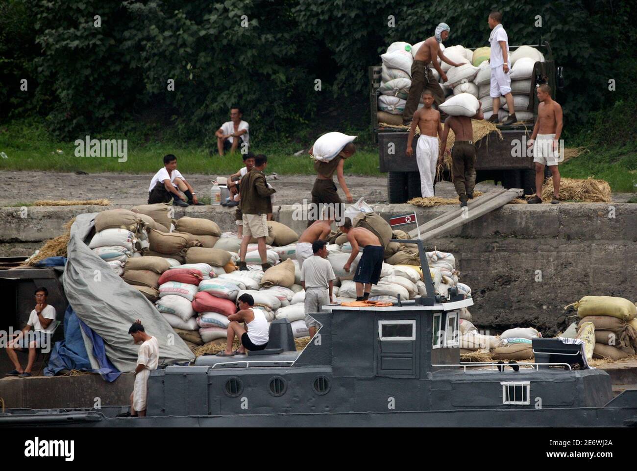 North Korean soldiers unload bags of corn from a cargo boat on the bank of the Yalu River near the North Korean town of Sinuiju August 4, 2009. Former U.S. President Bill Clinton arrived in North Korea on Tuesday to try to win the release of two jailed U.S. journalists, a move some analysts said could mark the isolated state's return to dialogue over nuclear weapons. REUTERS/Jacky Chen (NORTH KOREA MILITARY SOCIETY POLITICS IMAGES OF THE DAY) Stock Photo
