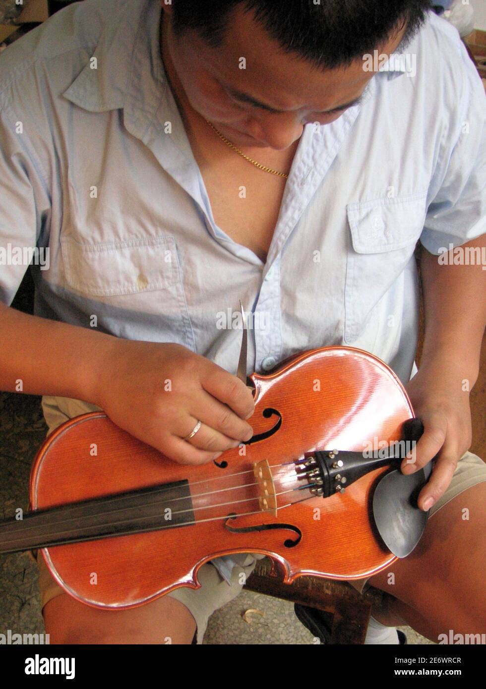 Zhang Chenjia puts the finishing touches on a violin at the Shanghai Lark Golden Bell Music Instruments workshop August 8, 2005. From bustling Shanghai to thriving Guangzhou, thousands of factories fashion up to 1 million instruments a year mostly bound for the U.S. and European markets, ranging from pedestrian students' violins to rarefied ones used in concerts that bear names like Andreas Eastman, Johannes Kohr and Andrew Schroetter. Picture taken August 8, 2005. To match feature LEISURE-CHINA-VIOLINS REUTERS/Jerker Hellstrom  CC/YH Stock Photo