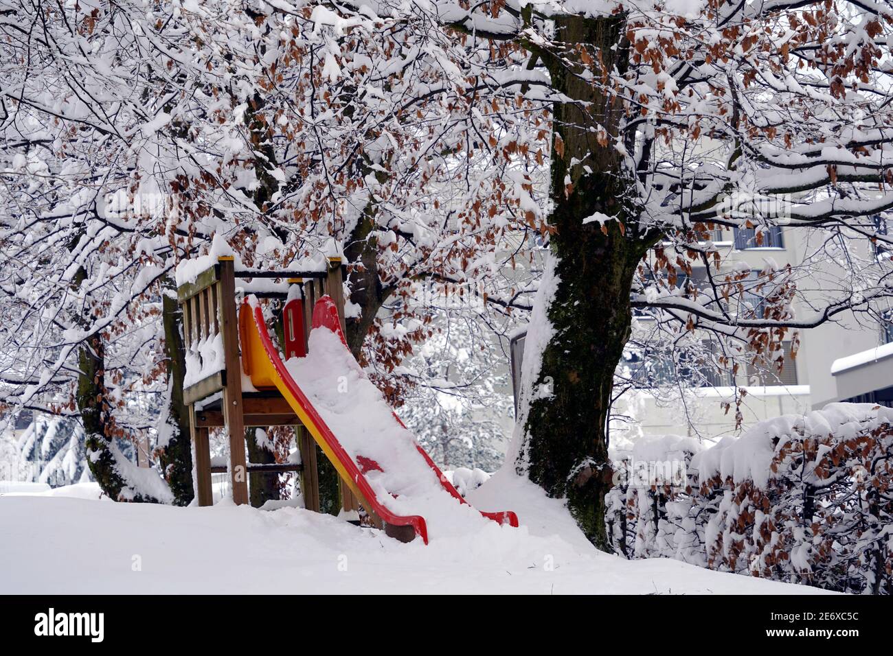 Garden in winter with a slide for children covered with snow. The branches of the trees around are under the snow as well. Example of heavy snowfall. Stock Photo