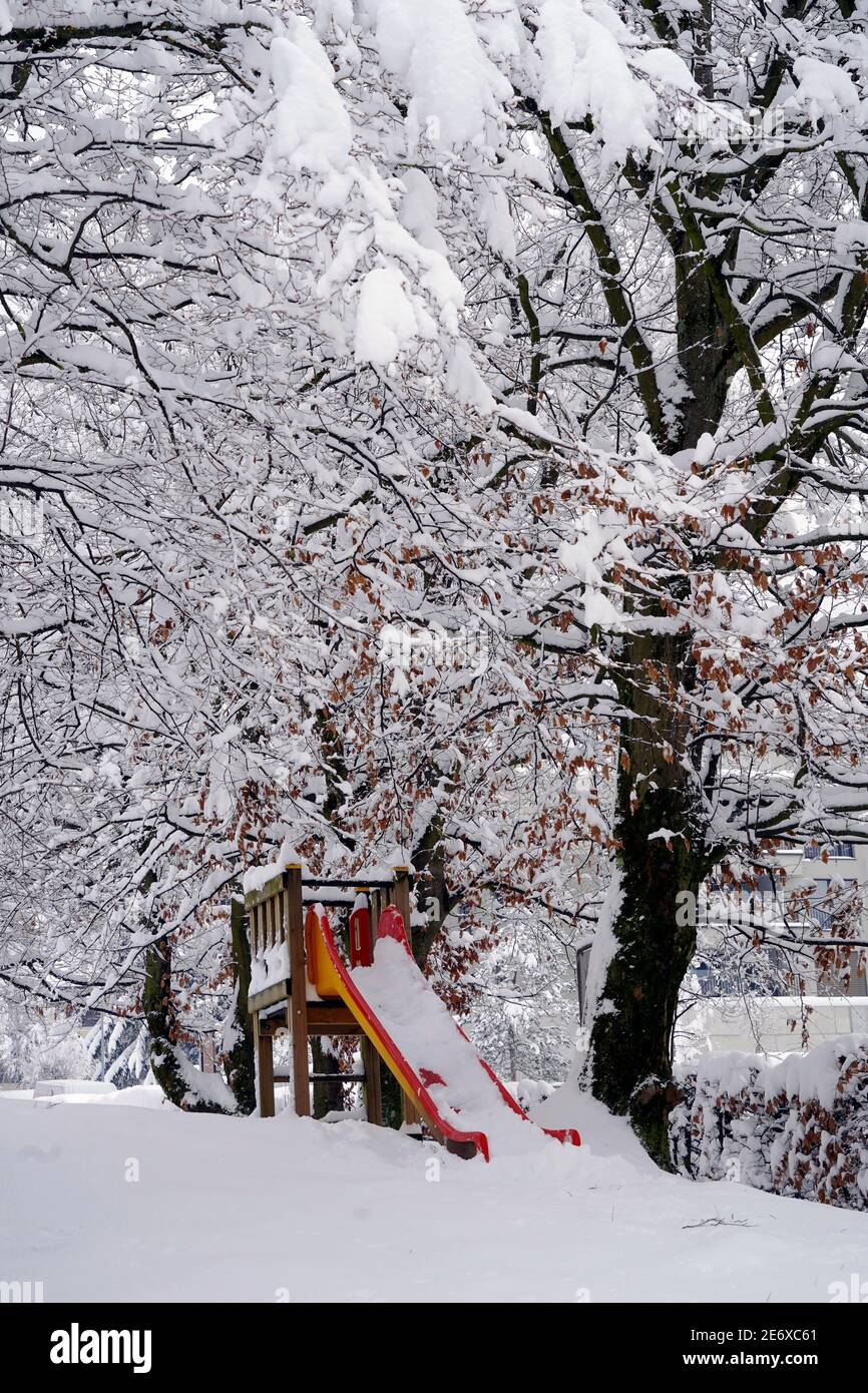 Garden in winter with a slide for children covered with snow in vertical view. The branches of the trees around are under the snow as well. Stock Photo