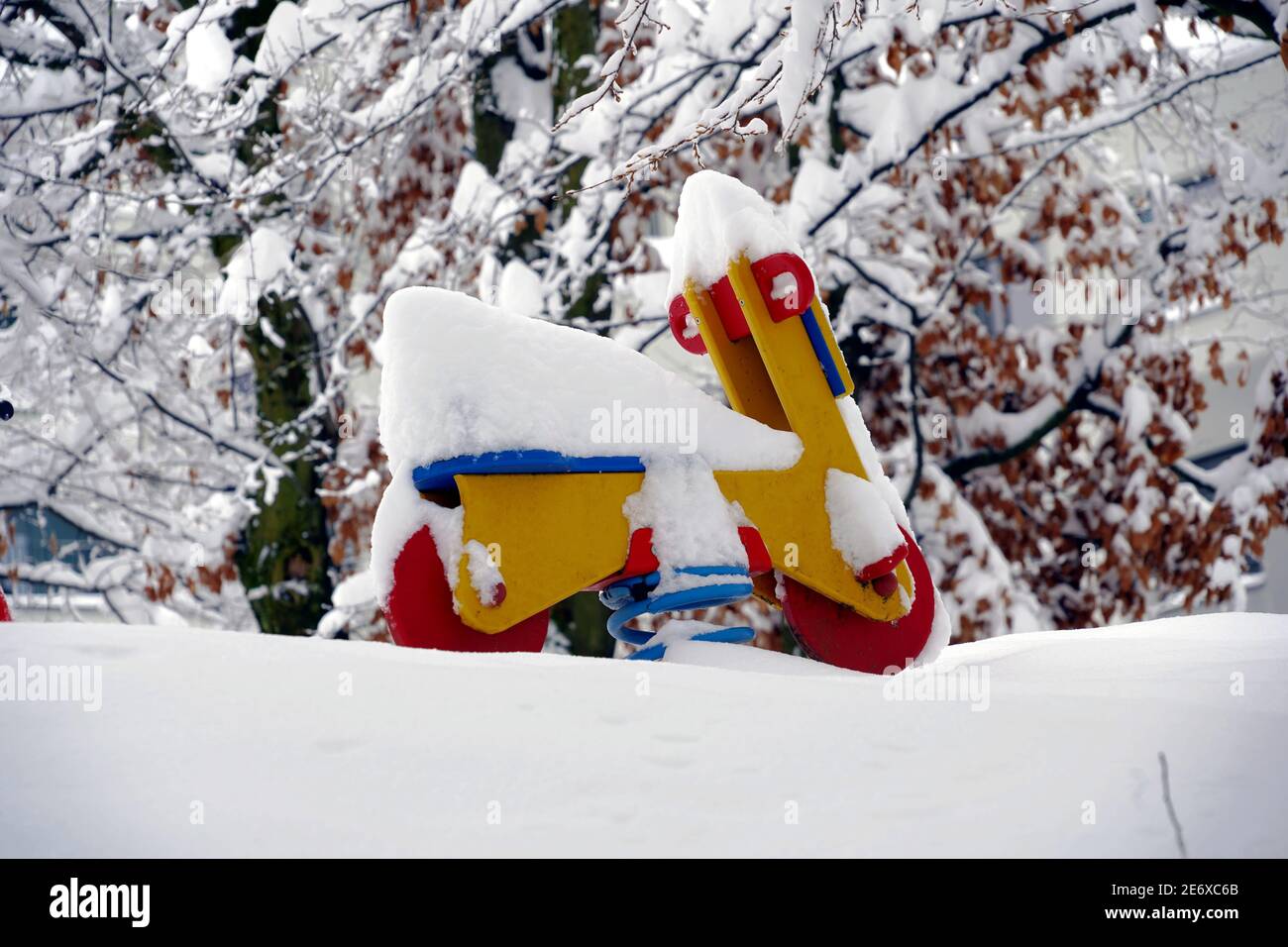 Rocking motorcycle on a spring, wooden toy in red and yellow  in garden in winter, with  snow covered trees on the background in extreme snowfall. Stock Photo