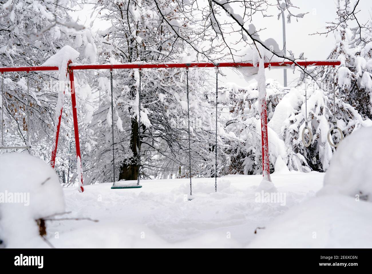 Swing for children in garden in winter, covered with snow, only silhouettes of red metal construction are visible as a result of extreme snowfall. Stock Photo