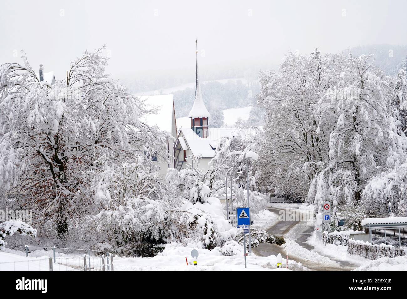 Old reformed church building in Urdorf, Switzerland in winter with a street and crossroad in foreground, all covered with snow after extreme snowfall Stock Photo