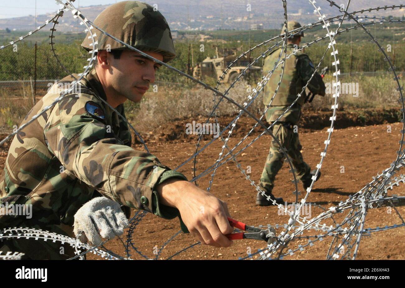 Lebanese soldiers clear away wires as Israeli soldiers in an army vehicle  keep watch (background) along the border with Israel in the Khiam valley in  south Lebanon October 24, 2006. The wires