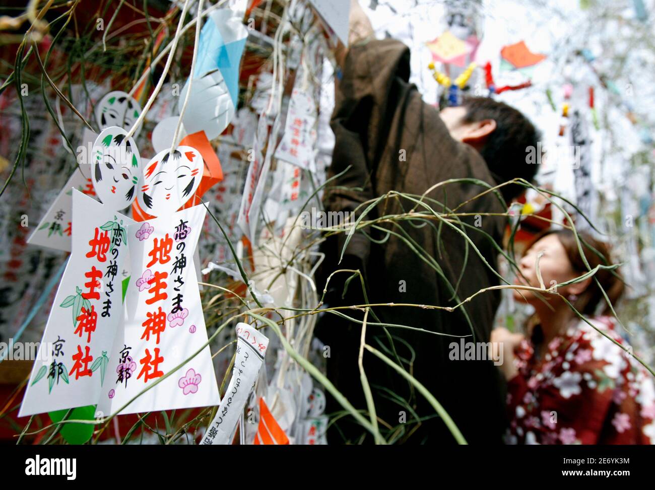 A Pair Of Paper Dolls Which Represent A Couple Are Seen On A Bamboo Branch While A Couple Hang Their Paper Dolls On A Branch For Good Luck In Love During Tanabata