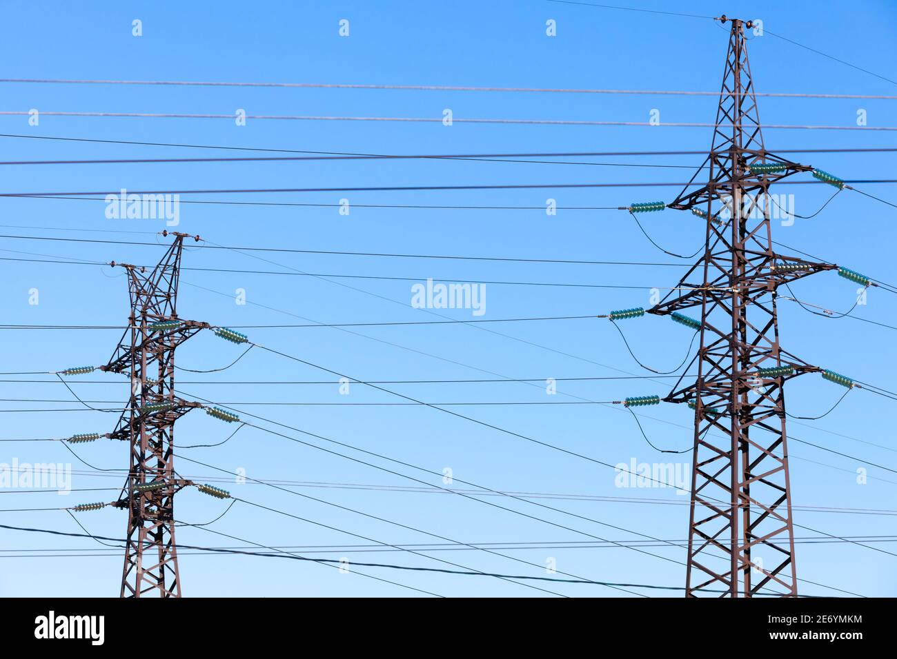 Lattice-type steel towers over blue sky as a part of high-voltage line. Overhead power line structures Stock Photo