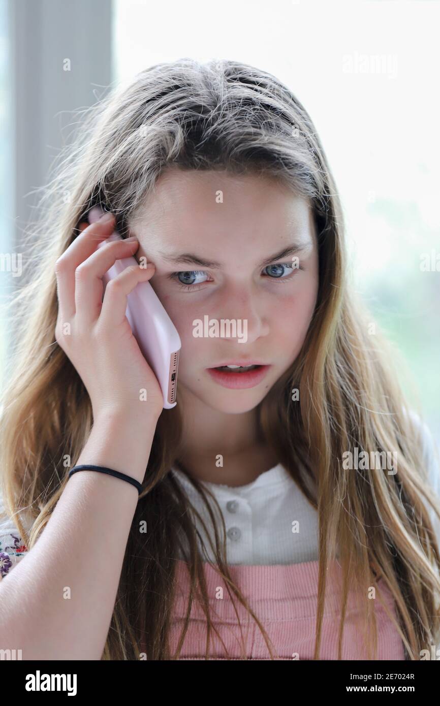 Young expressive beautiful brunette preteen with long hair and brown eyes talking on cellphone with pink case expressing a look of disbelief and doubt Stock Photo