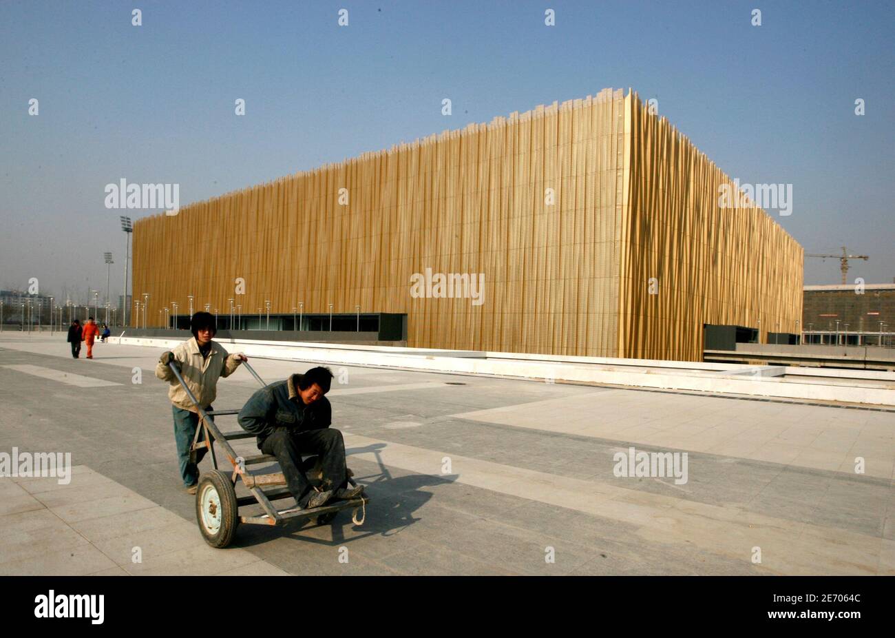 A worker carries a trolley past the Beijing Olympic Basketball Gymnasium in Beijing January 15, 2008. The 18,000-seat venue has been shrouded in straw-coloured aluminium after officials decided at the last moment that the jade-coloured frosted opaque glass of the original design was 'dull and tedious'.  Picture taken on  January 15, 2008. REUTERS/Jason Lee (CHINA) Stock Photo