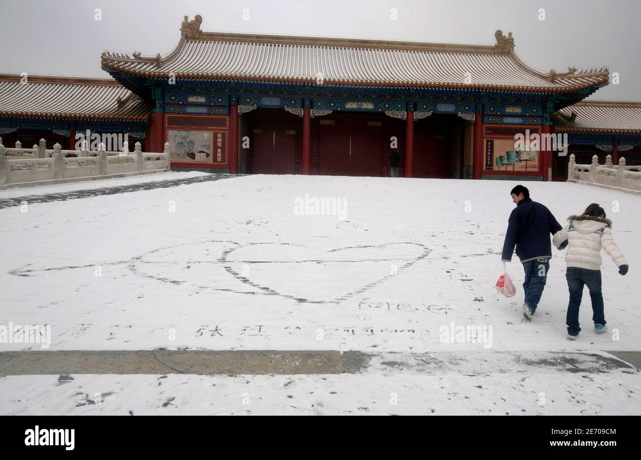 A couple walk away after drawing hearts in the snow inside the Forbidden City, after a snowfall in Beijing February 18, 2009. China took credit on Tuesday for the first snowfall of the winter in Beijing, saying it fired sticks of chemicals into the sky to seed clouds in a bid to end a persistent drought. REUTERS/Jason Lee (CHINA) Stock Photo