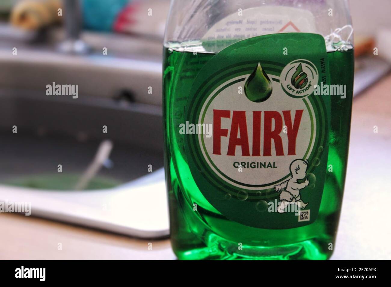 A bottle of fairy washing up liquid in front of a kitchen sink filled with dishes Stock Photo