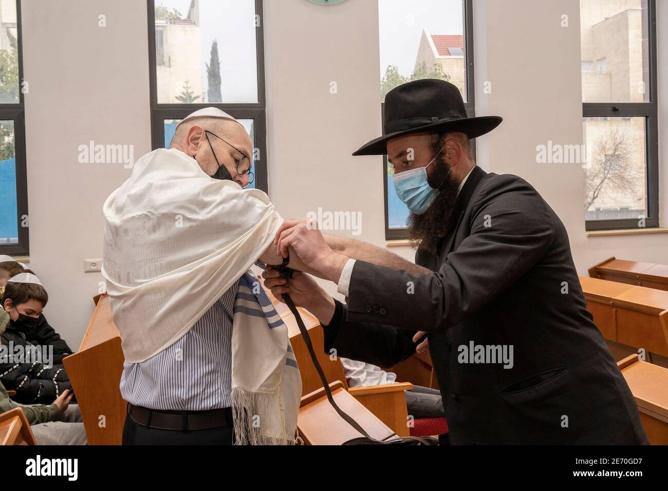 Jerusalem, Israel - January 28th, 2020: A rabbi helps a man with his tefillin in a synagogue, both wearing protective masks Stock Photo