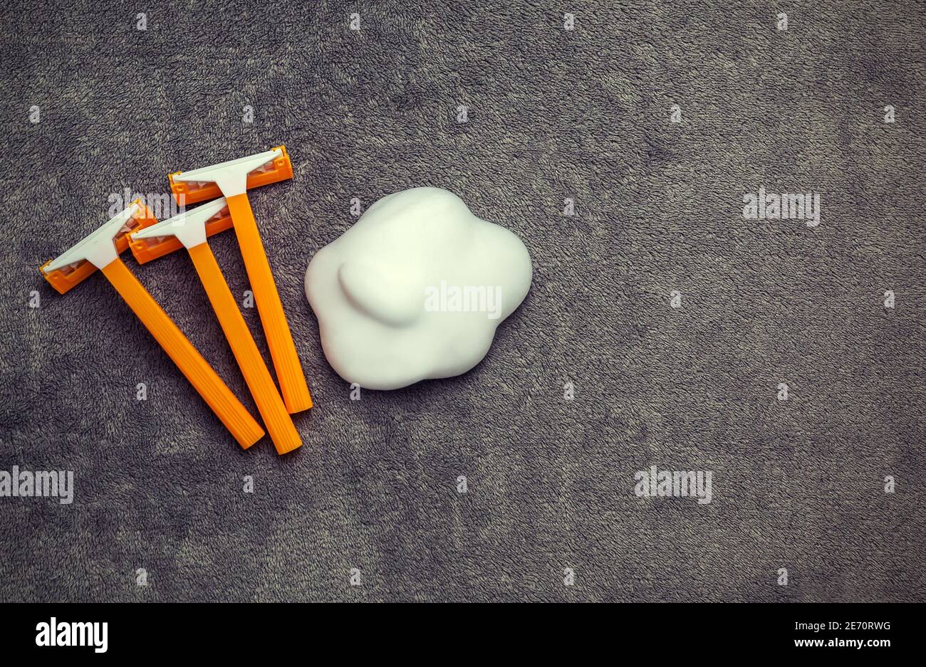 Orange disposable shavers razors with shaving cream in cloud shape at grey background Stock