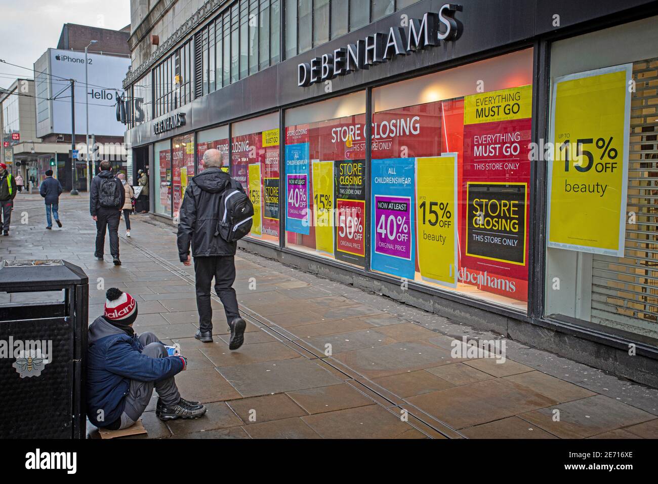 Store closing sign outside the Debenhams shop in Manchester  city centre, with people passing homeless man begging . Stock Photo