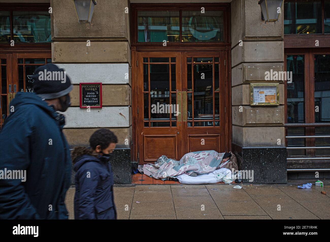 Homeless man sleeps in pub doorway with passing by mother and child  in Manchester . Stock Photo