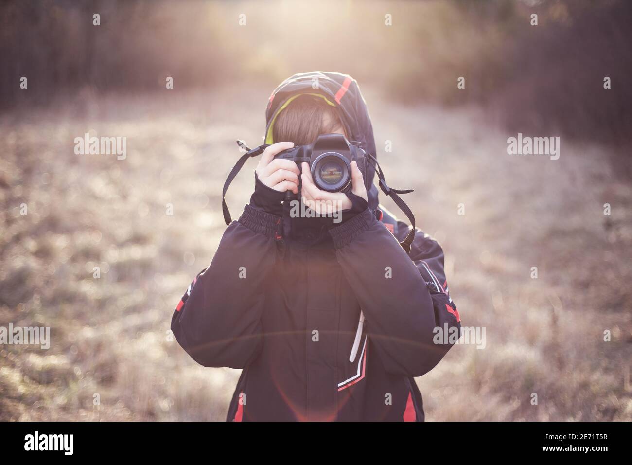 Boy child photographer learning photography, taking a photo, holding a professional dslr camera in front of his face. Stock Photo