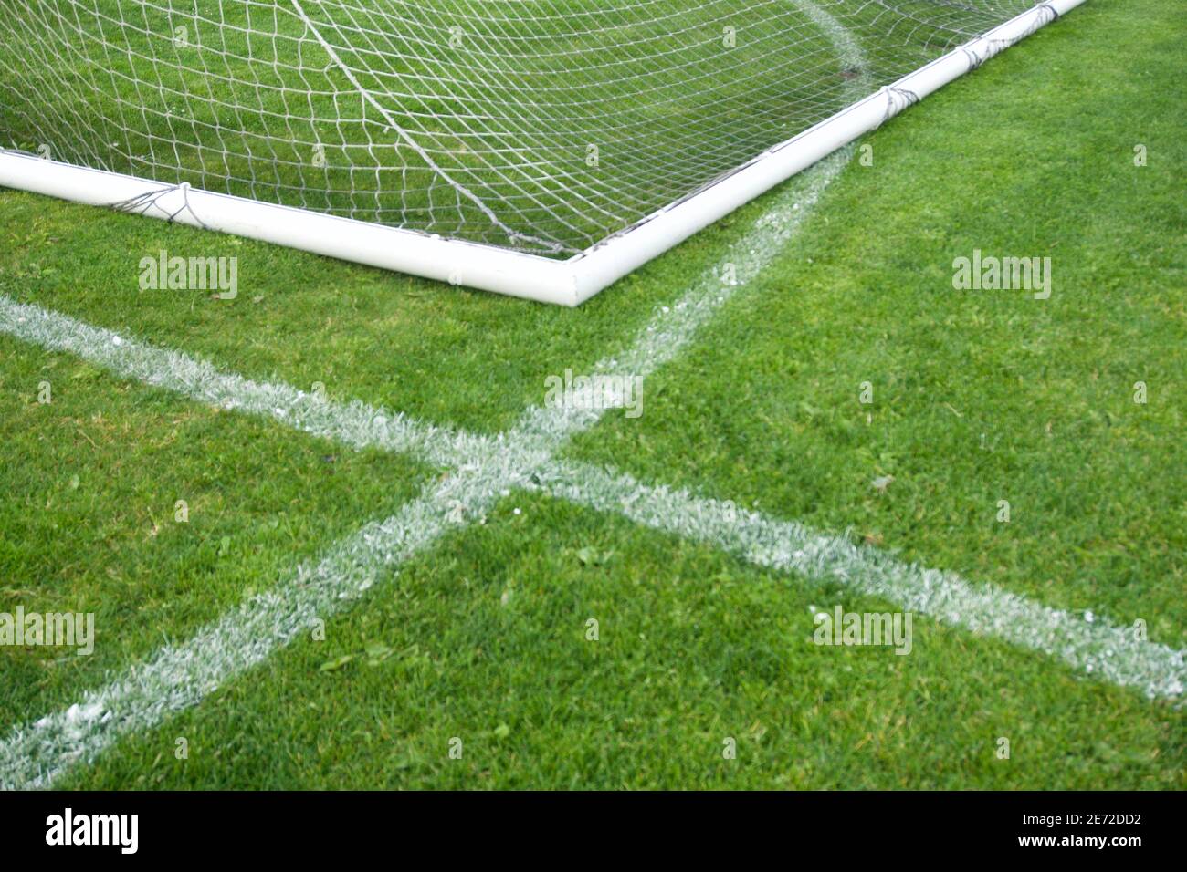 Green grass painted with a white 'x' lawn paint for goal and game boundary markings, with white soccer goal frame, twine mesh, and tubing. Stock Photo