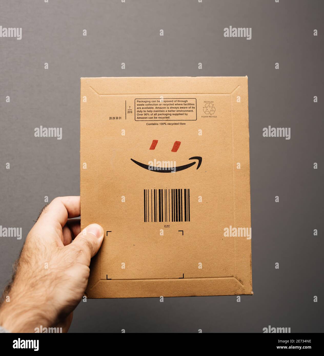 Paris, France - Oct 29, 2018: POV male hand holding Amazon Prime parcel envelope with smile logo and add red eyes to form a smiling human character Stock Photo