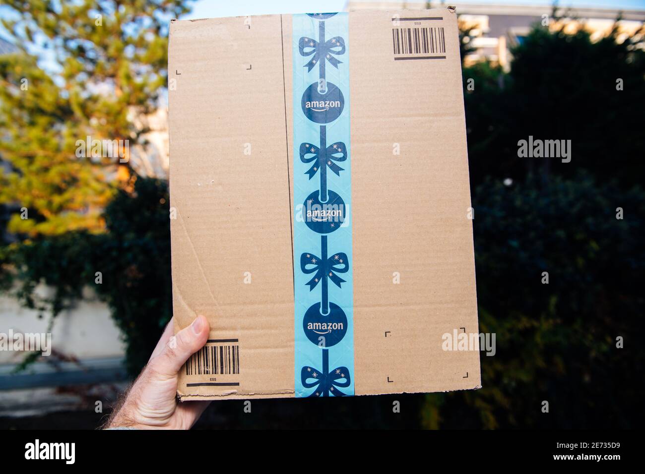 Paris, France - Nov 16, 2018: Point of view male hand holding showing Amazon Prime cardboard with festive holiday scotch tape - defocused city background Stock Photo