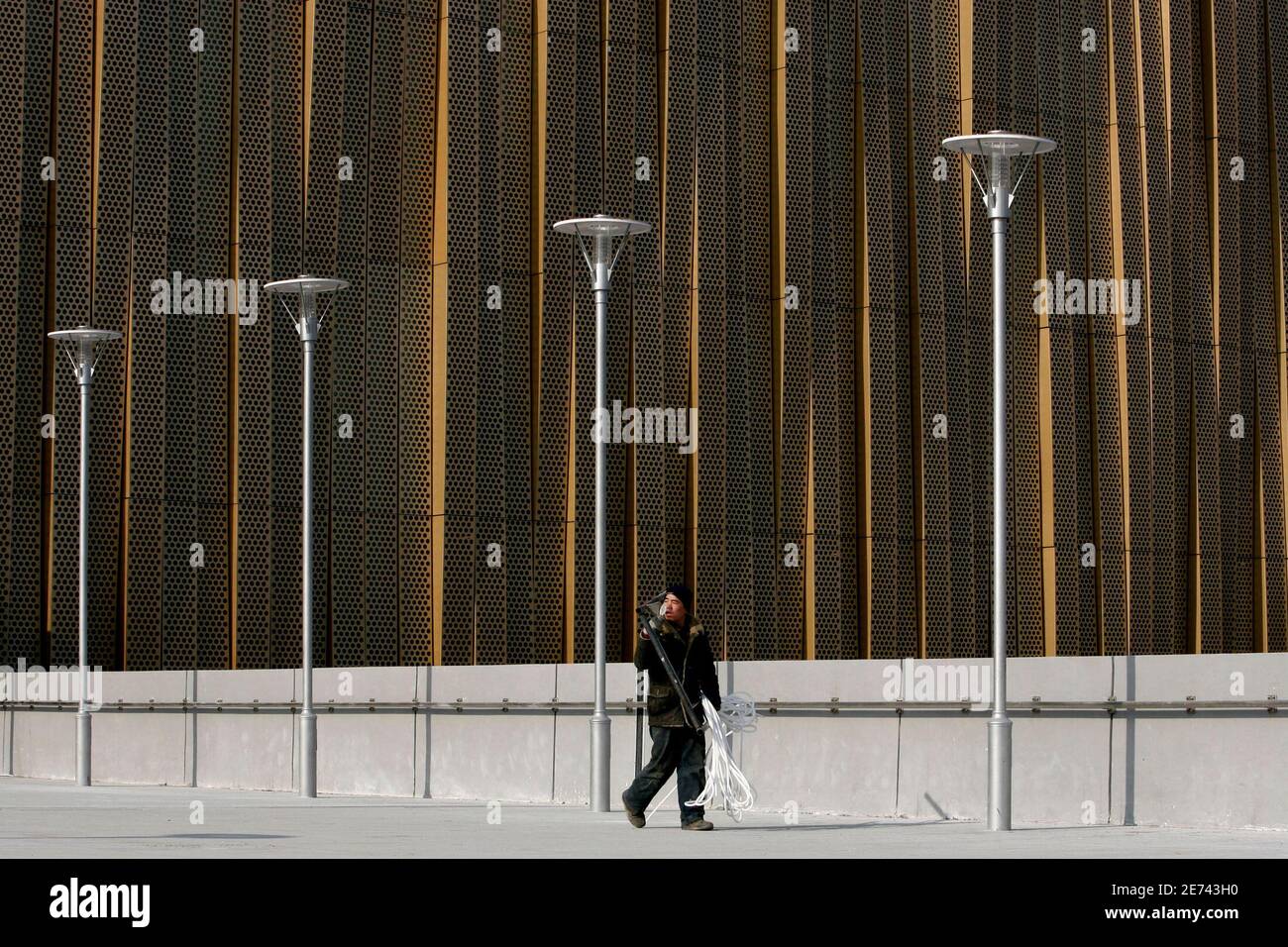 A worker walks outside the Beijing Olympic Basketball Gymnasium in Beijing January 15, 2008. The 18,000-seat venue has been shrouded in straw-coloured aluminium after officials decided at the last moment that the jade-coloured frosted opaque glass of the original design was 'dull and tedious'.  Picture taken January 15, 2008. REUTERS/Jason Lee (CHINA) Stock Photo