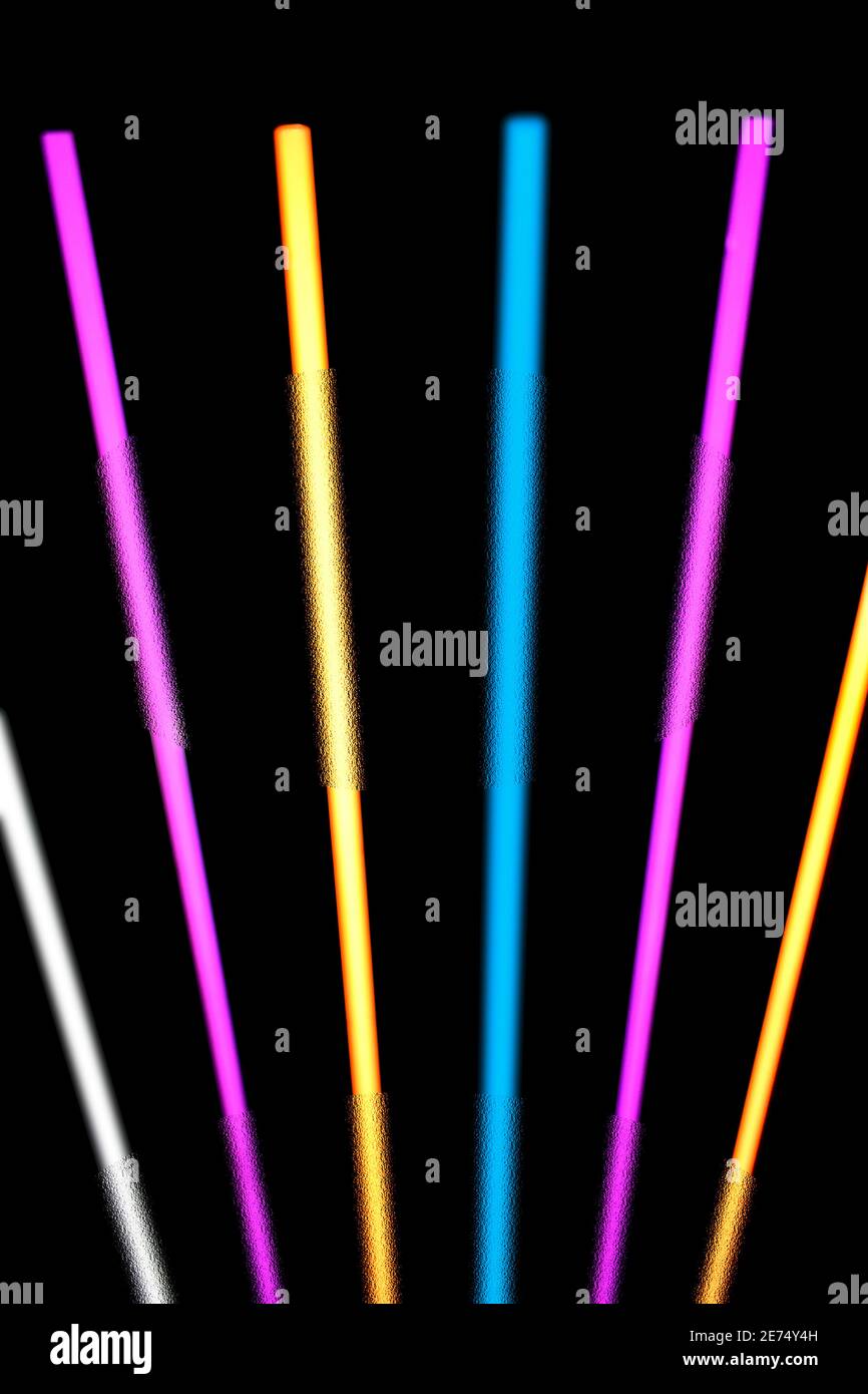 Glowing neon light strips in pink, yellow, blue and white against a black background. Stock Photo