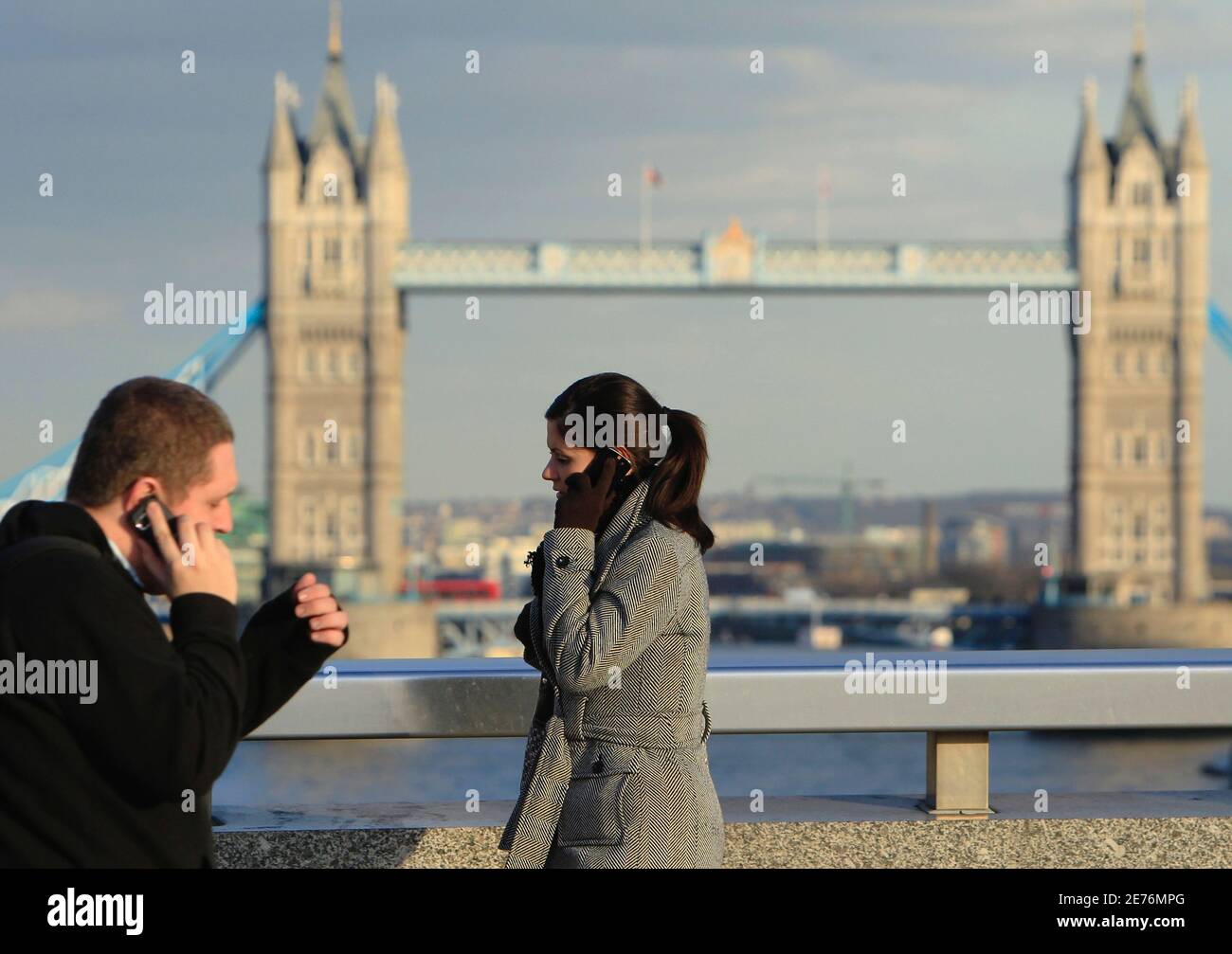 Two people pass each other talking on mobile telephones in front of Tower  Bridge whilst walking accross London Bridge in London March 1, 2010. France  Telecom's Orange and Deutsche Telekom's T-Mobile won