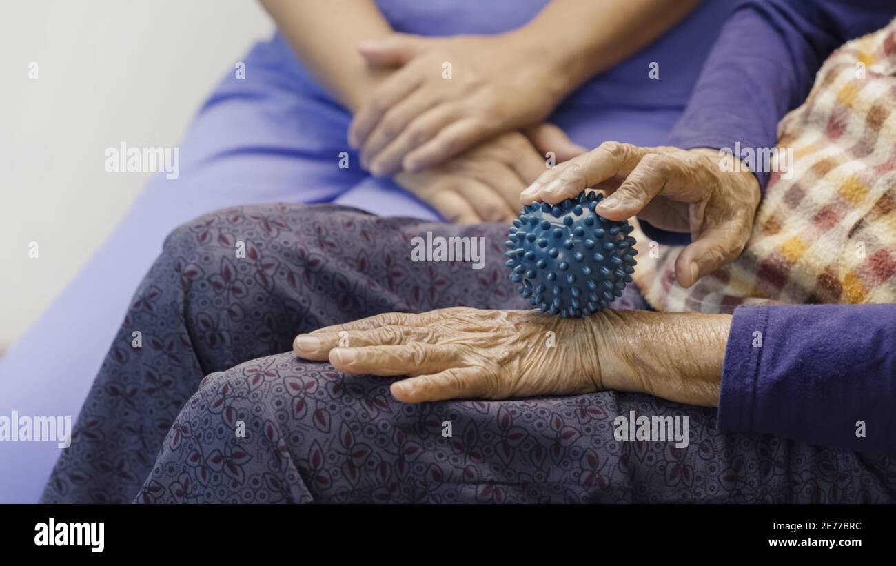 Elderly woman doing rubber ball for exercise fingers, palm ,hand and foot muscle with caregiver take care. Stock Photo