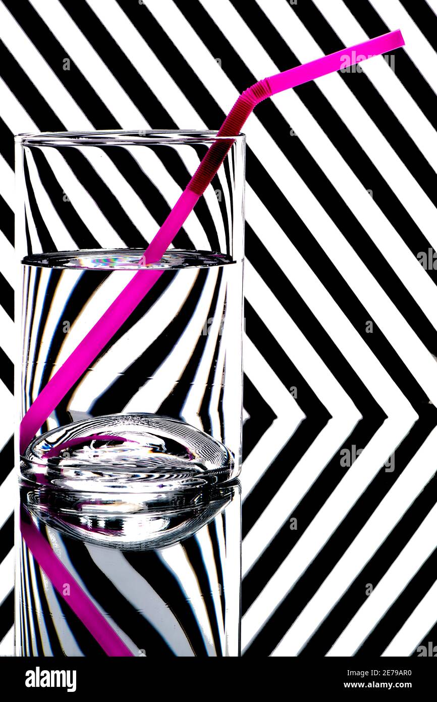 refraction of light by a glass on a black and white striped background with drinking straw. Abstract glass art. Stock Photo