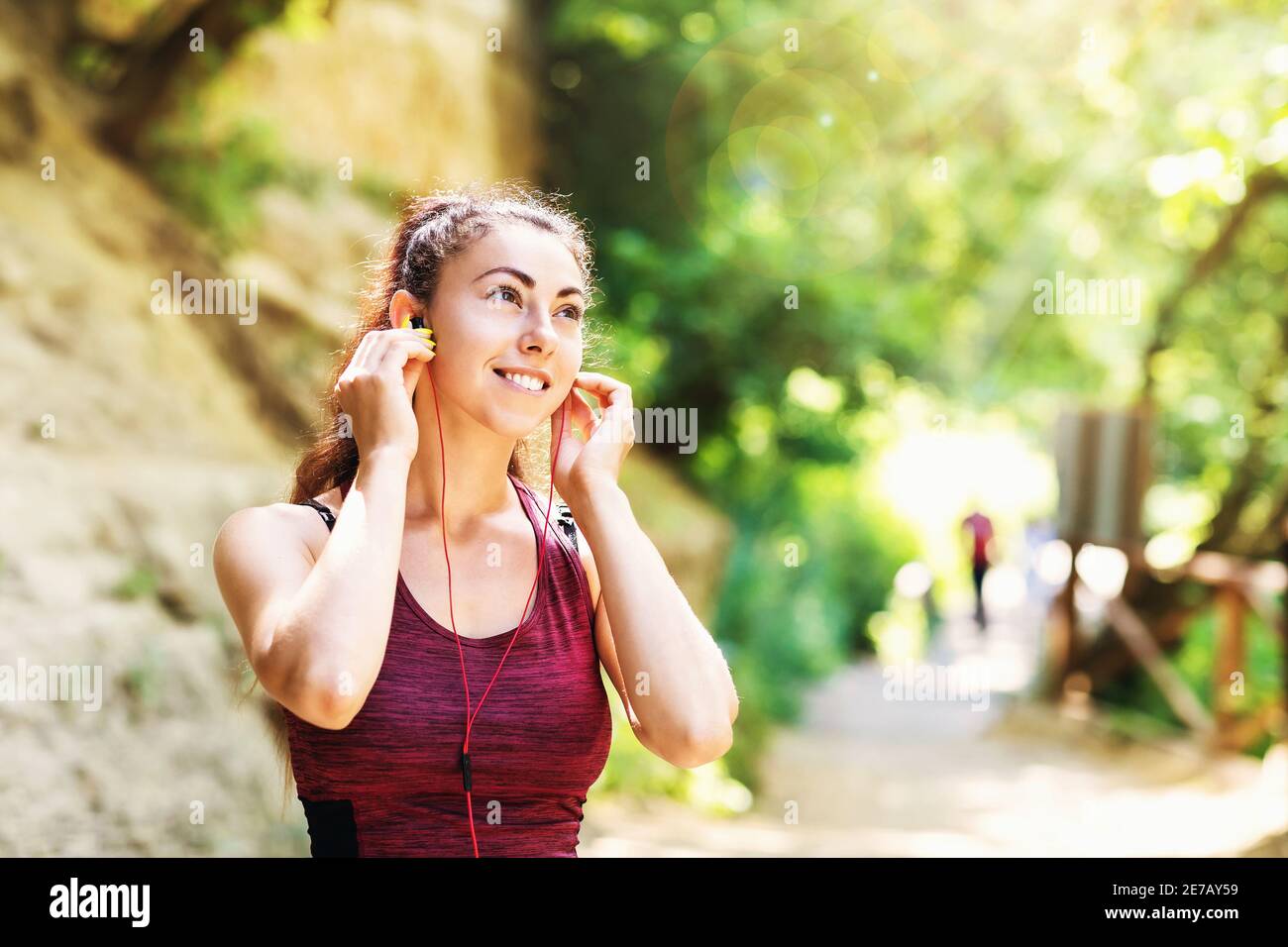 Young contented woman in sportswear in the park listens to music on headphones while exercising on the street. Healthy lifestyle concept. Stock Photo