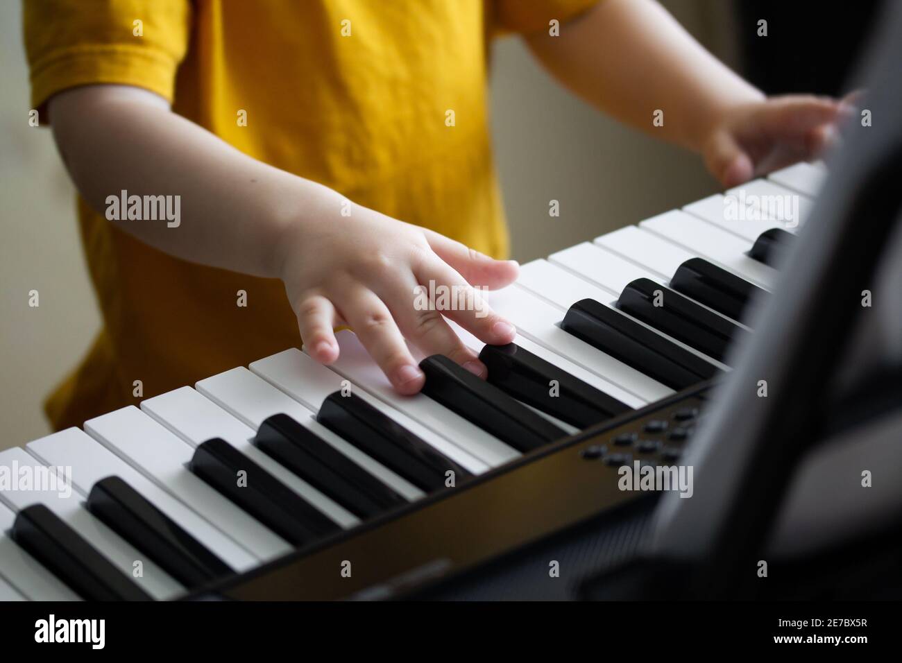 Child's hands on the synthesizer's keyboard. Toddler learning how to play piano. Small fingers pressing on the keys closeup. Early development and edu Stock Photo