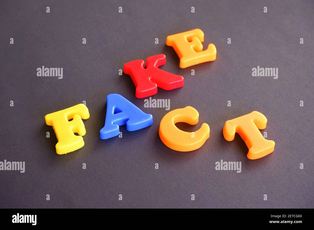 Fake and fact words in colorful plastic magnetic letters on a dark grey black background Stock Photo