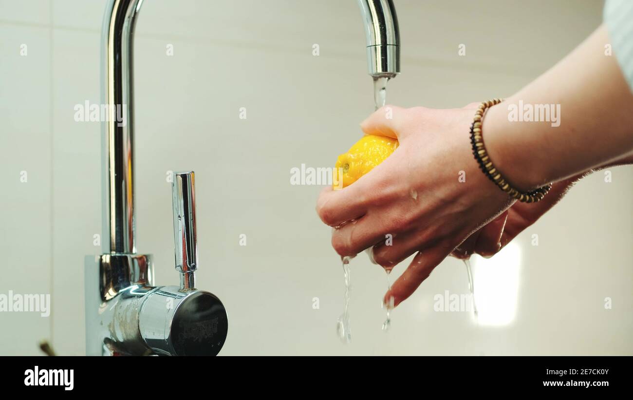 Woman's hands wash a lemon under the tap with water. Washing fruits