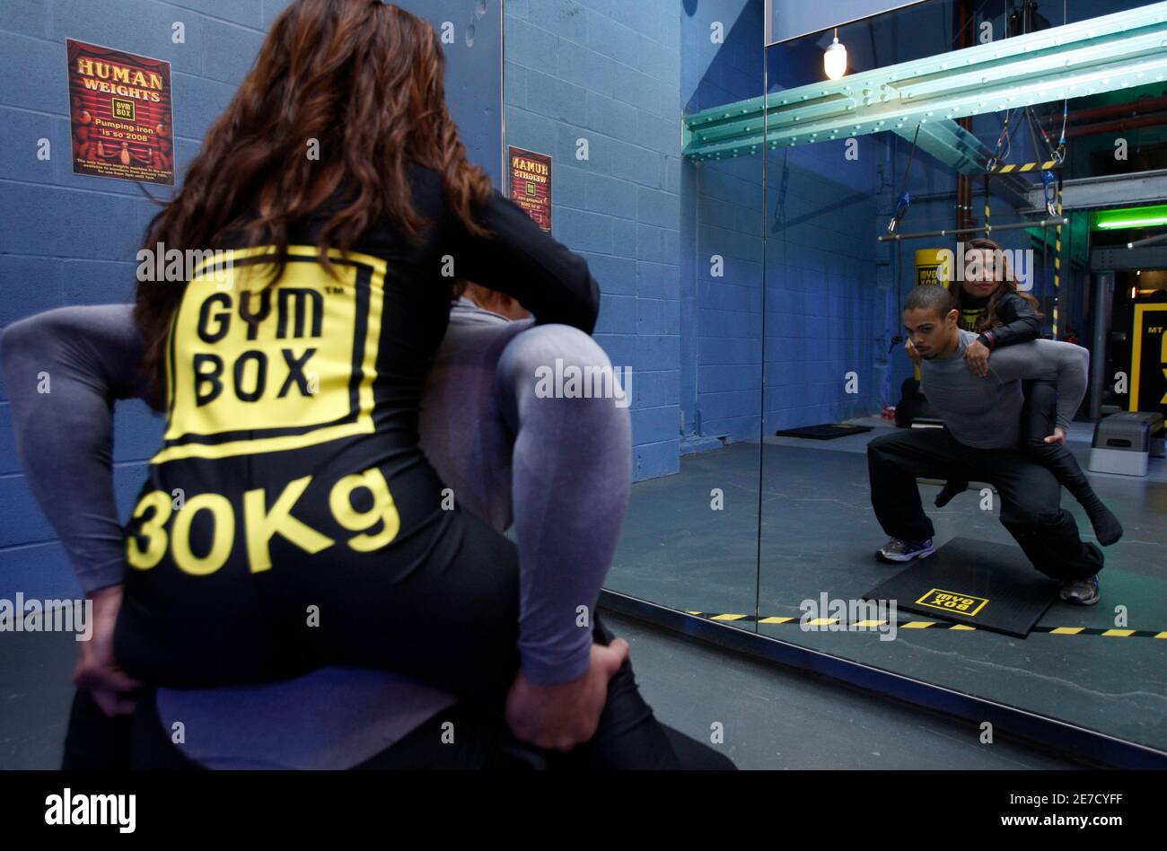A fitness instructor does some squat exercises for photographers using a human weight at a Gymbox gym in London January 21, 2009. A British gym is trying to add human interest to otherwise dreary workouts by replacing traditional dumbbell weights with human ones.The Gymbox chain gym in central London says fitness enthusiasts can now swap their usual lumps of metal for human beings in a range of shapes and sizes.   REUTERS/Stephen Hird   (BRITAIN) Stock Photo