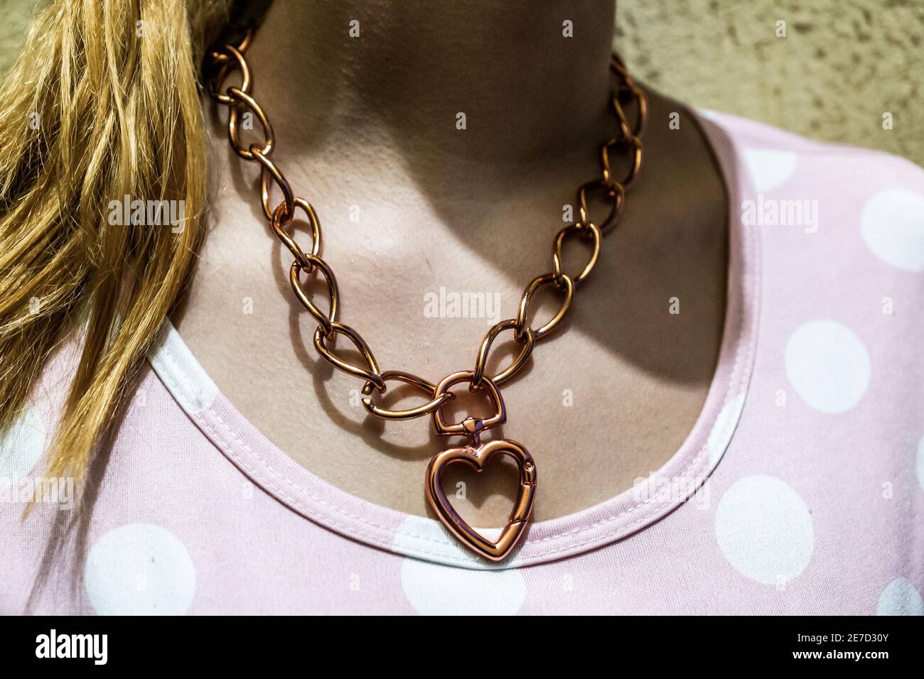 Closeup of a female's neck wearing a chain necklace with a heart pen