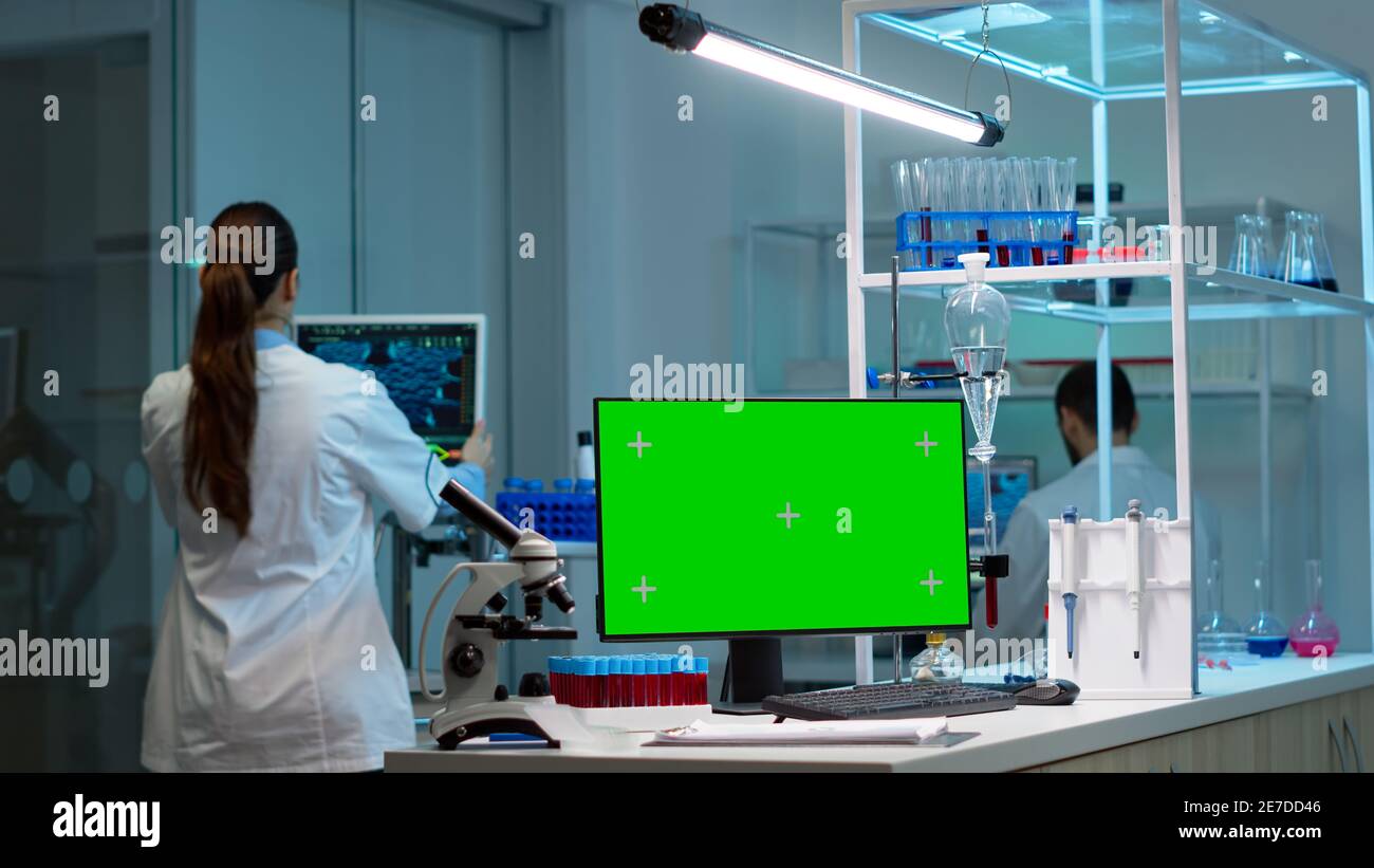Team of scientists working in background of modern laboratory using computer with green screen