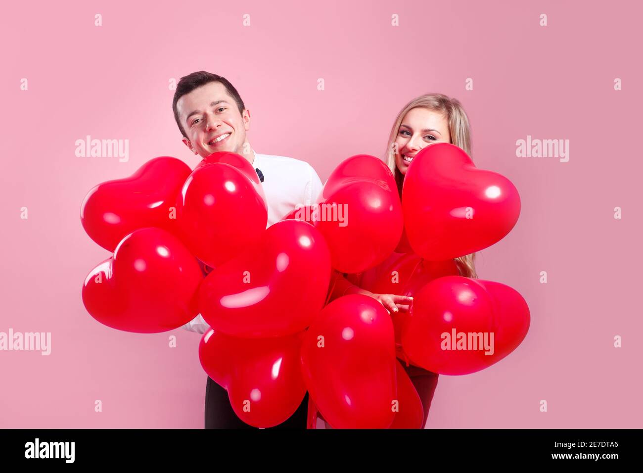 Valentines day. Surprised young couple with balloons heart on pink ...