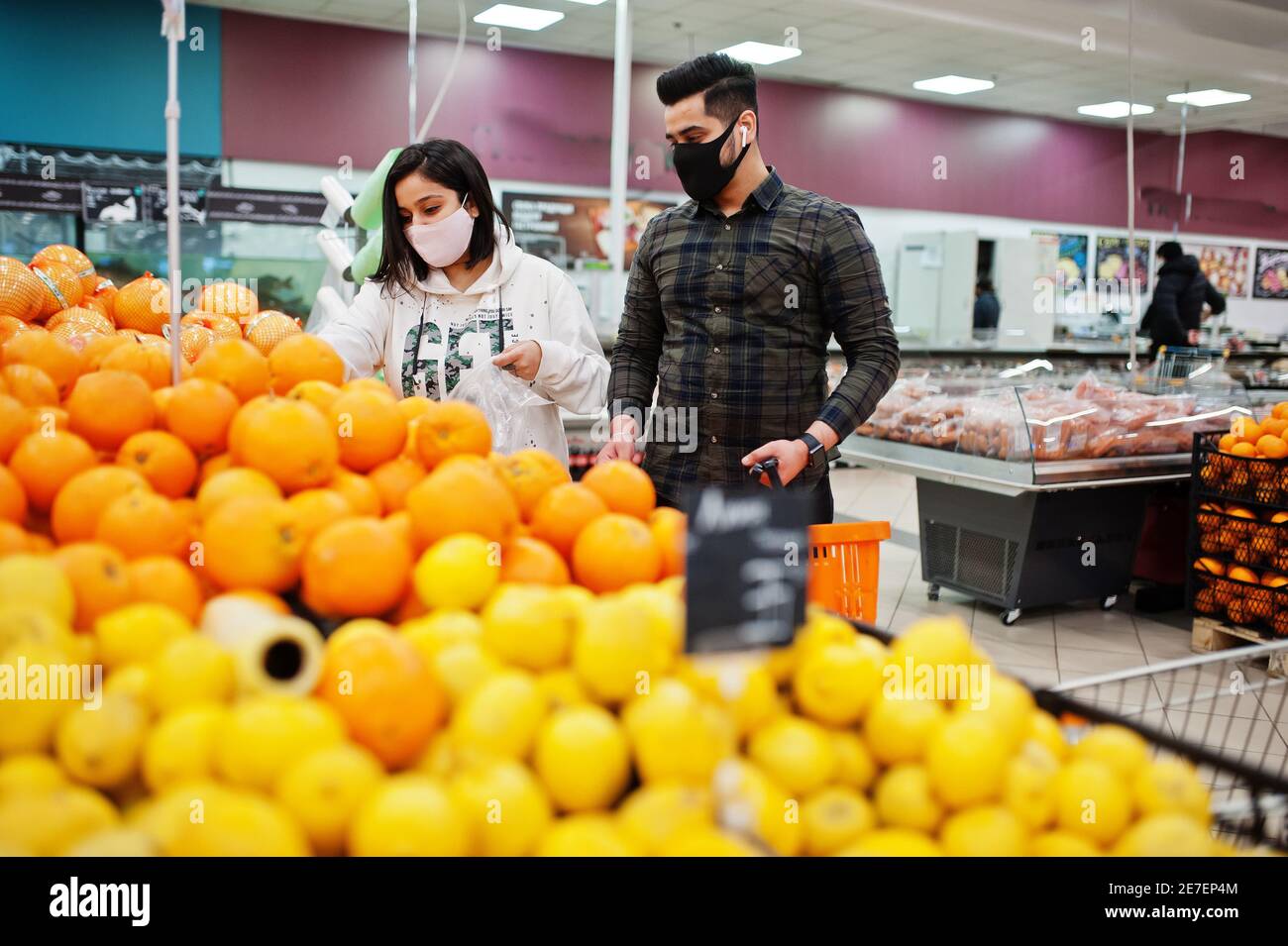 Asian couple wear in protective face mask shopping together in supermarket during pandemic. Choosing different fruits. Stock Photo