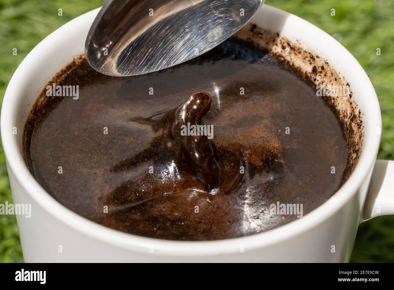 A teaspoon is adding ingredient into a cup of coffee with splash on