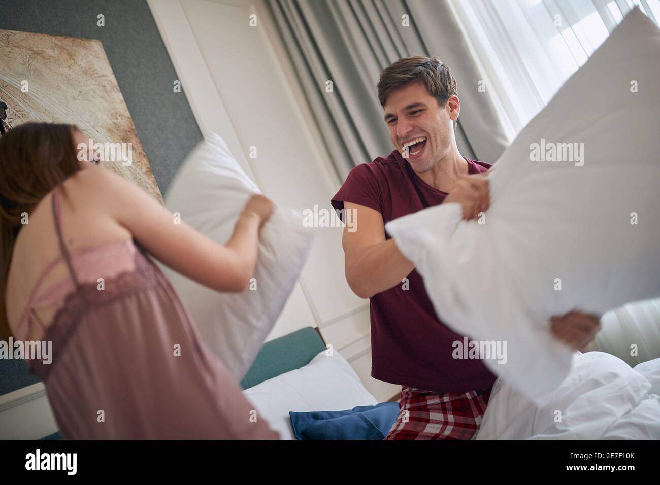A young couple at the hotel room enjoying pillow fight in the bed on a beautiful morning. Couple, love, hotel, together Stock Photo