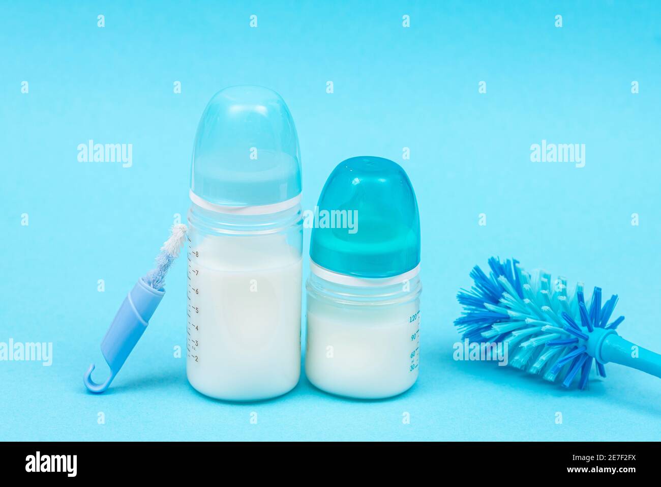 Baby bottles with milk and nipples bottle brush accessories on blue background. Baby products, symbols for newborns Stock Photo