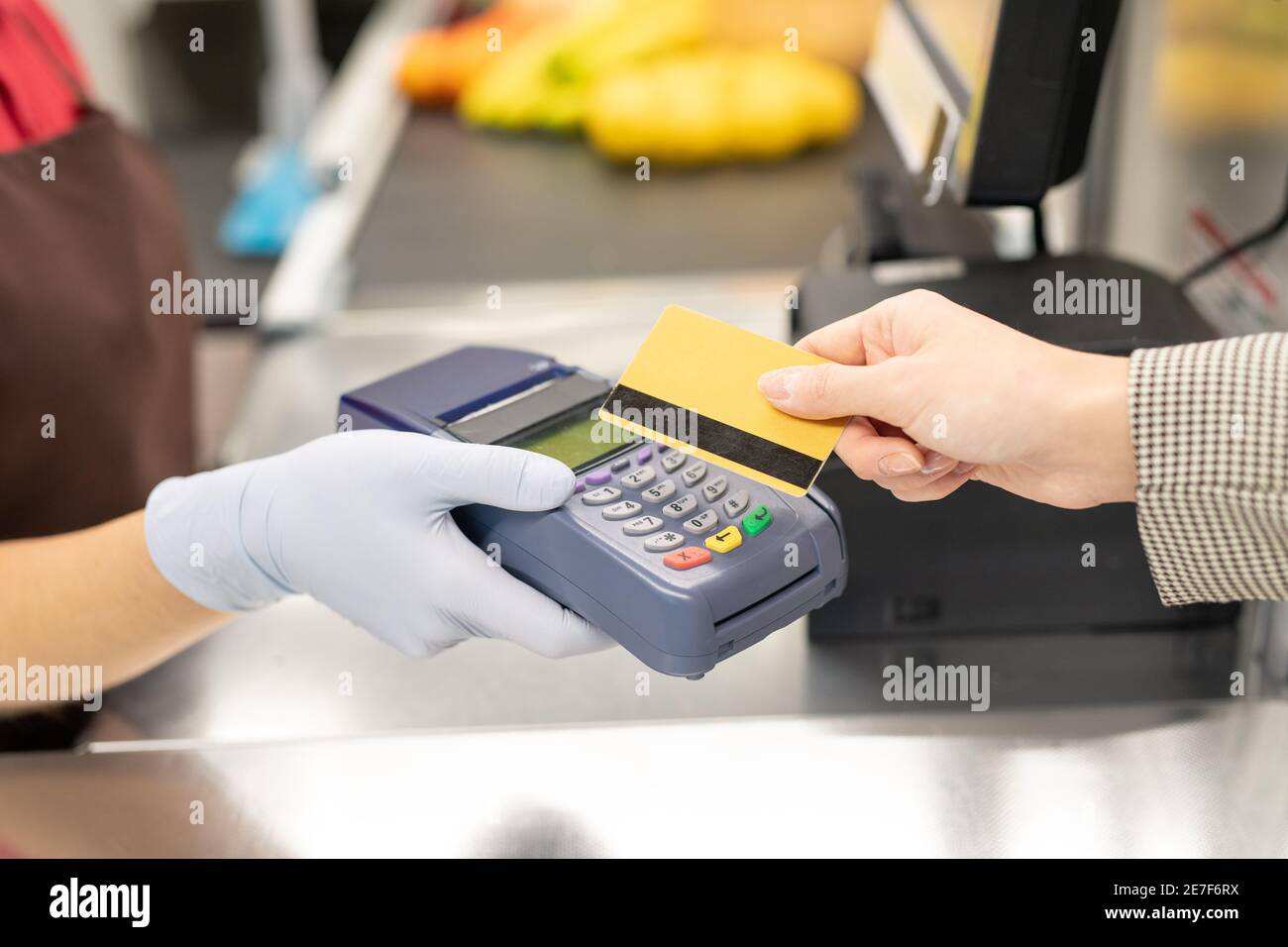 Hand of young female cashier in uniform and protective gloves holding payment terminal while one of consumers paying by credit card Stock Photo