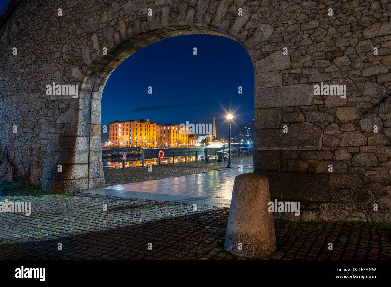 The Albert Dock viewed through stone arch at night, Liverpool, Merseyside Stock Photo