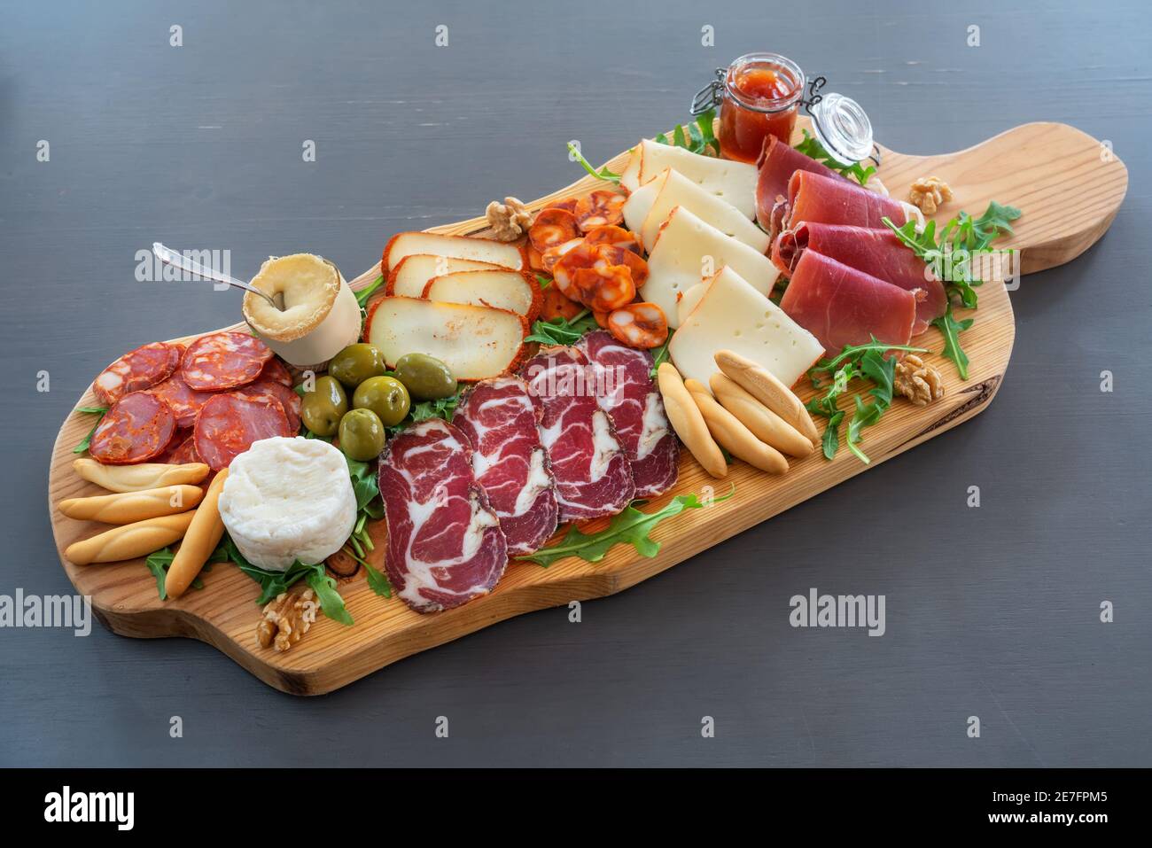 Very colorful tapas board of charcuterie with cheese and smoked meats. Decorated with arugula and walnuts. Stock Photo