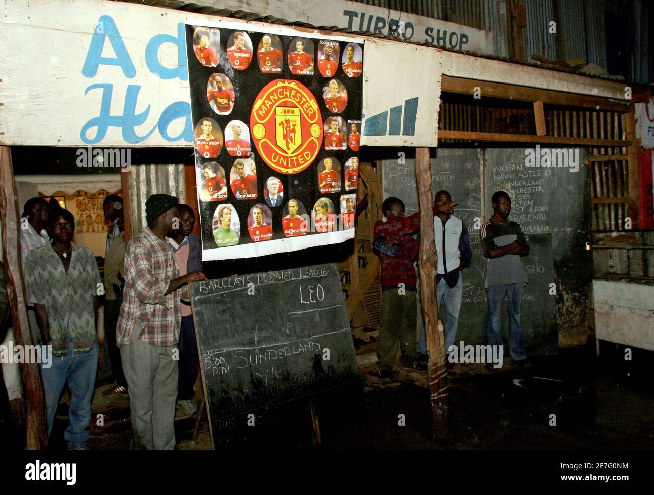 Kenyans stand outside a room where the Sunderland versus Manchester United match is being shown on television in Nairobi, October 15, 2005. It is Saturday afternoon in the Nairobi slum of Kawangware and up a narrow staircase through a low door into a dark room the atmosphere is wild. When Wayne Rooney scores for Manchester United, dozens of people -- shadows in the flicker of a television screen -- leap into the air, slap each others' backs and bang so hard on the corrugated iron walls that the flimsy building shakes. Picture take October 15, 2005. To match feature Kenya-Soccer REUTERS/Thomas  Stock Photo