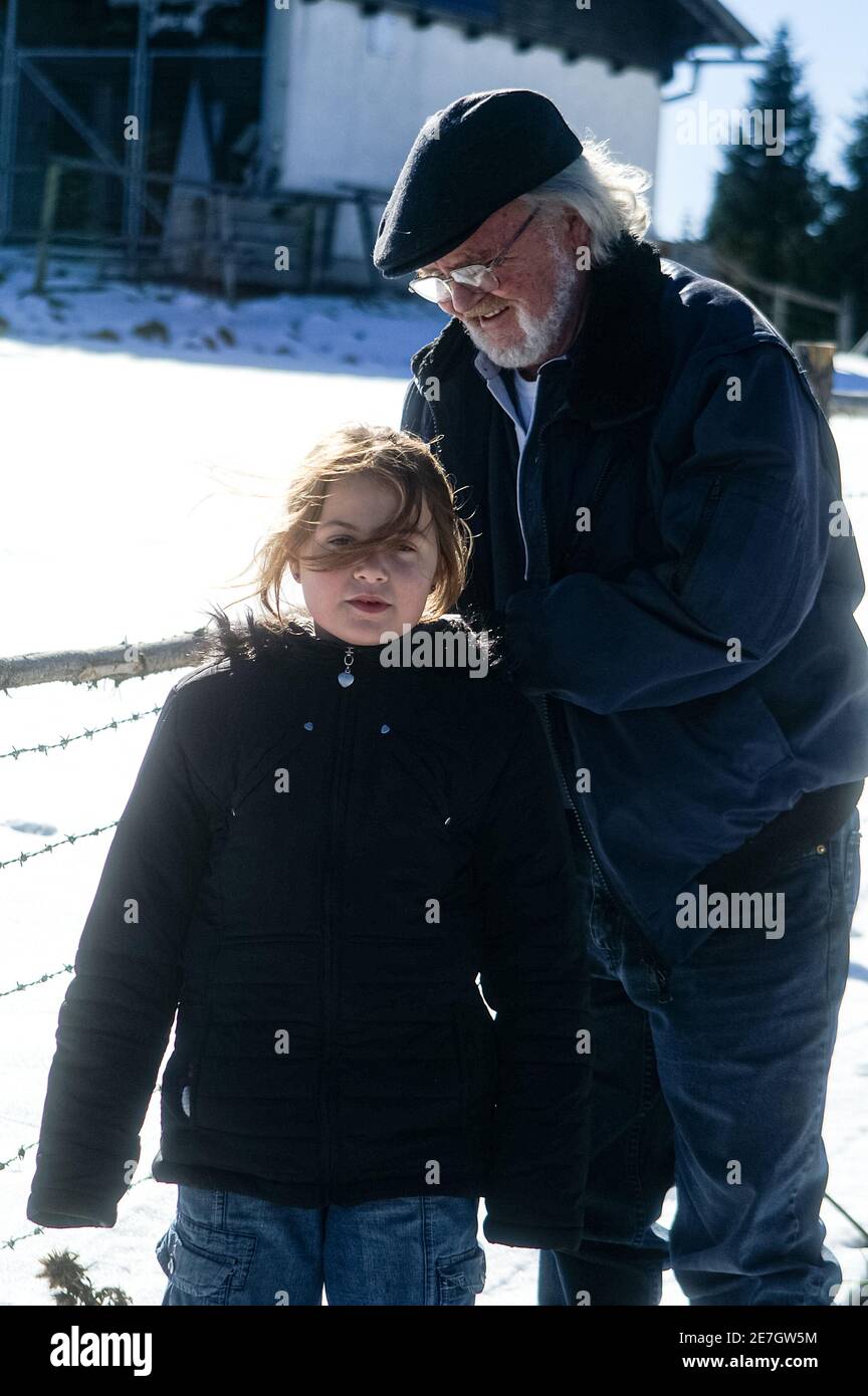 A grandfather adjusting the coat of his grandaughter on a snowy day Stock Photo