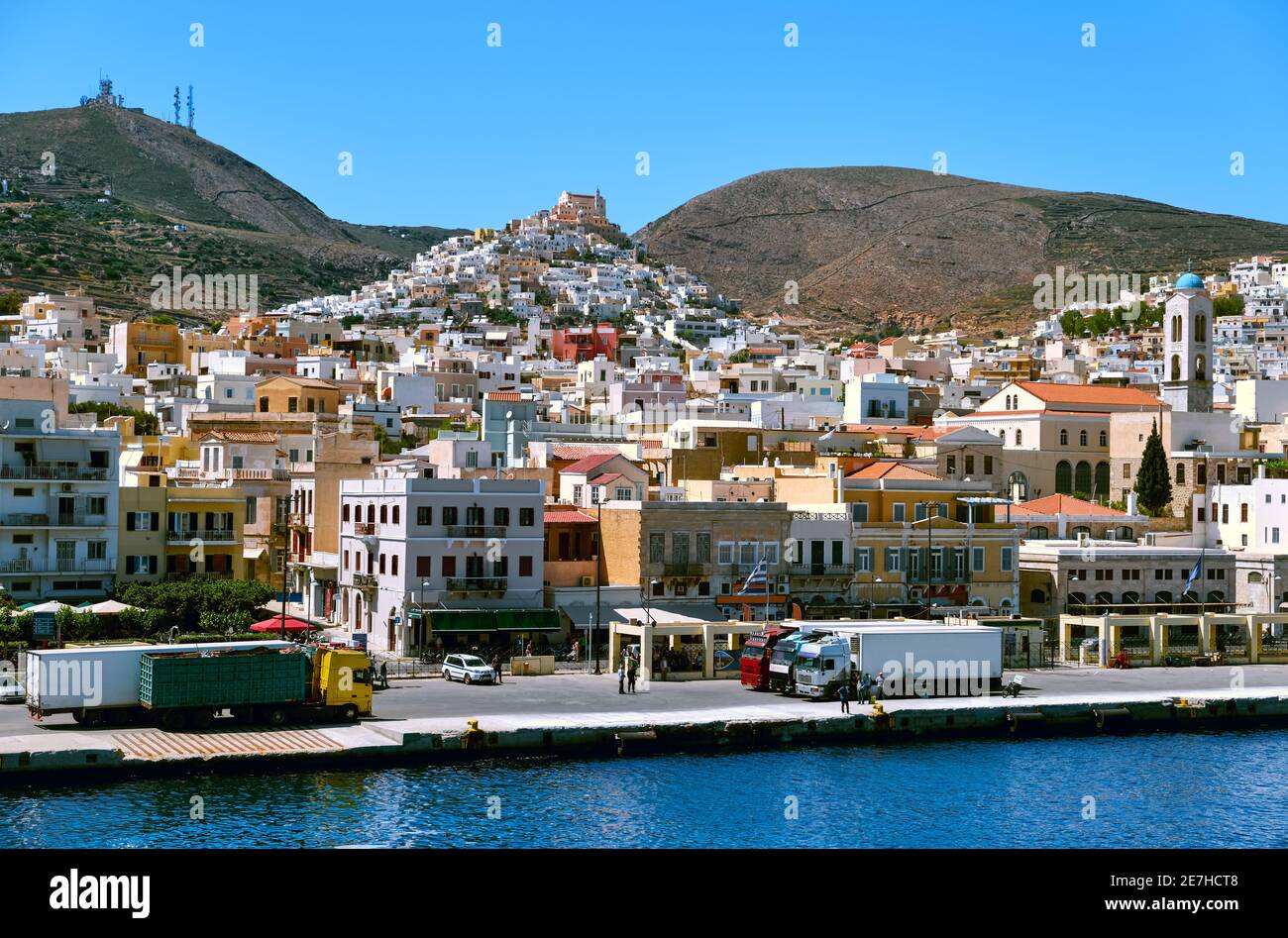 Ano Syros town, Syros island, Greece, St George catholic cathedral above, colorful houses, summer sun, trucks in port of Ermoupoli, Mediterranean sea. Stock Photo